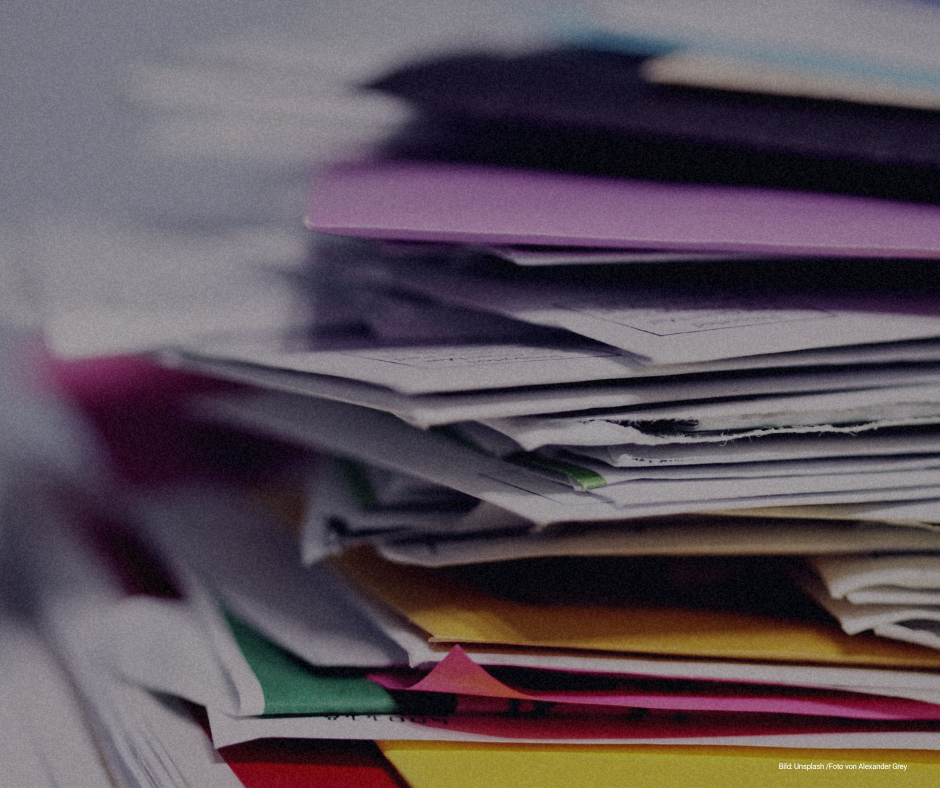 Verschiedenfarbige Akten stapeln sich übereinander. Bild: Unsplash / Alexander Grey.